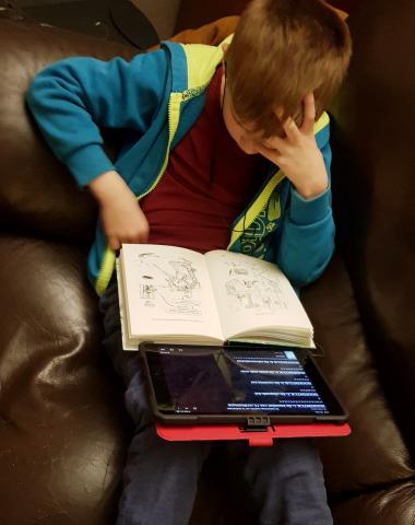Jongen leest in een boek en luistert tegelijk naar de Daisy-versie op zijn tablet
