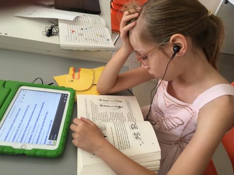Een meisje leest in een boek en luistert tegelijk naar het Daisy-luisterboek op haar tablet